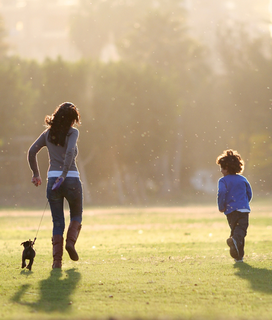 Woman holding a puppy while playing with a kid in the field