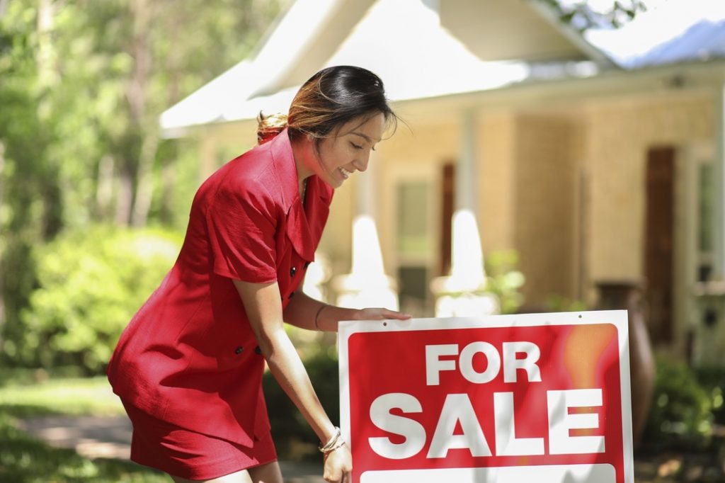 Woman putting a For Sale sign in front of a house