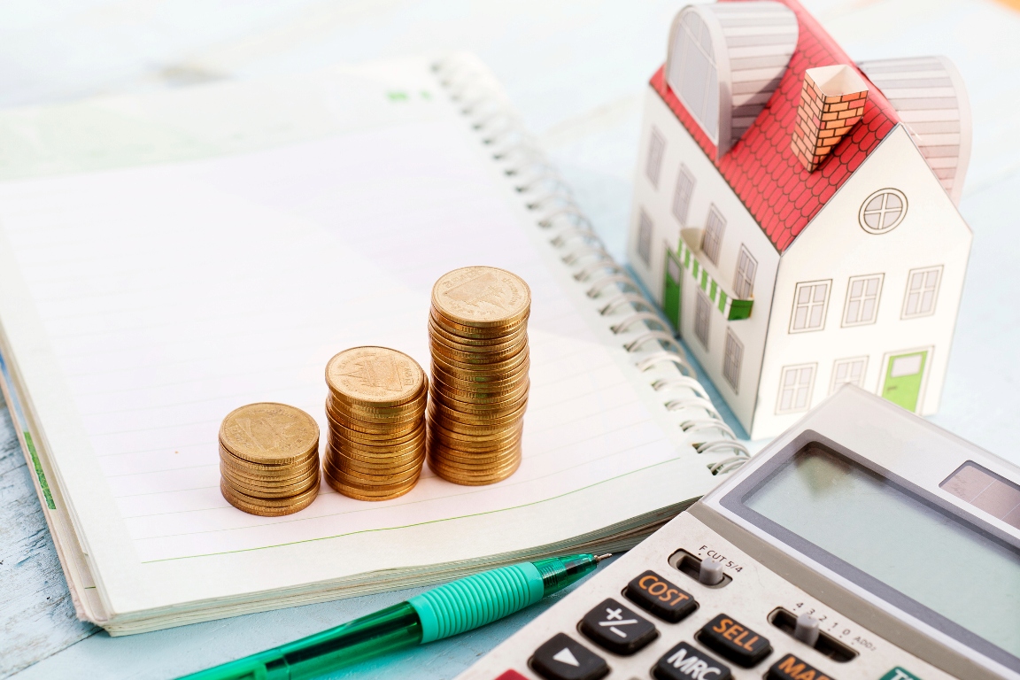 Notebook, calculator, miniature home model, and coins placed on a table 